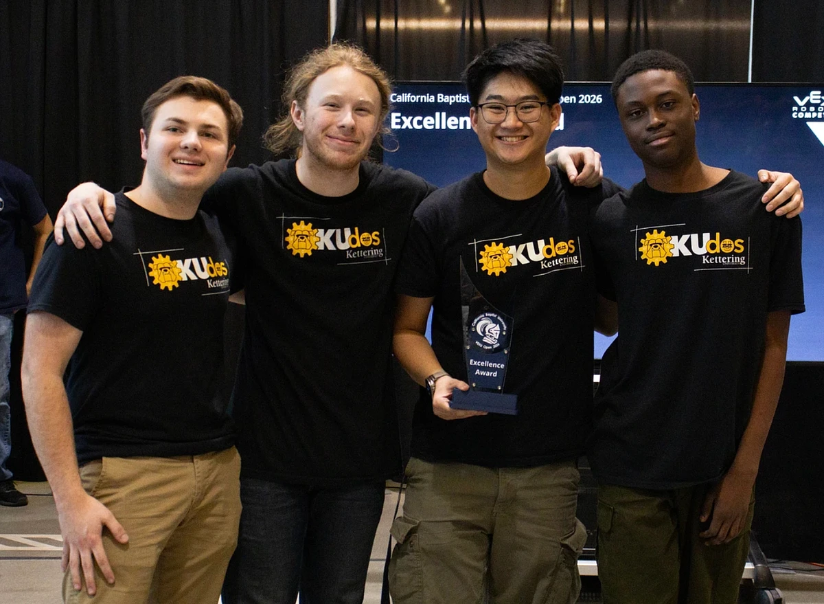 Four people wearing matching shirts pose with an "Excellence Award."